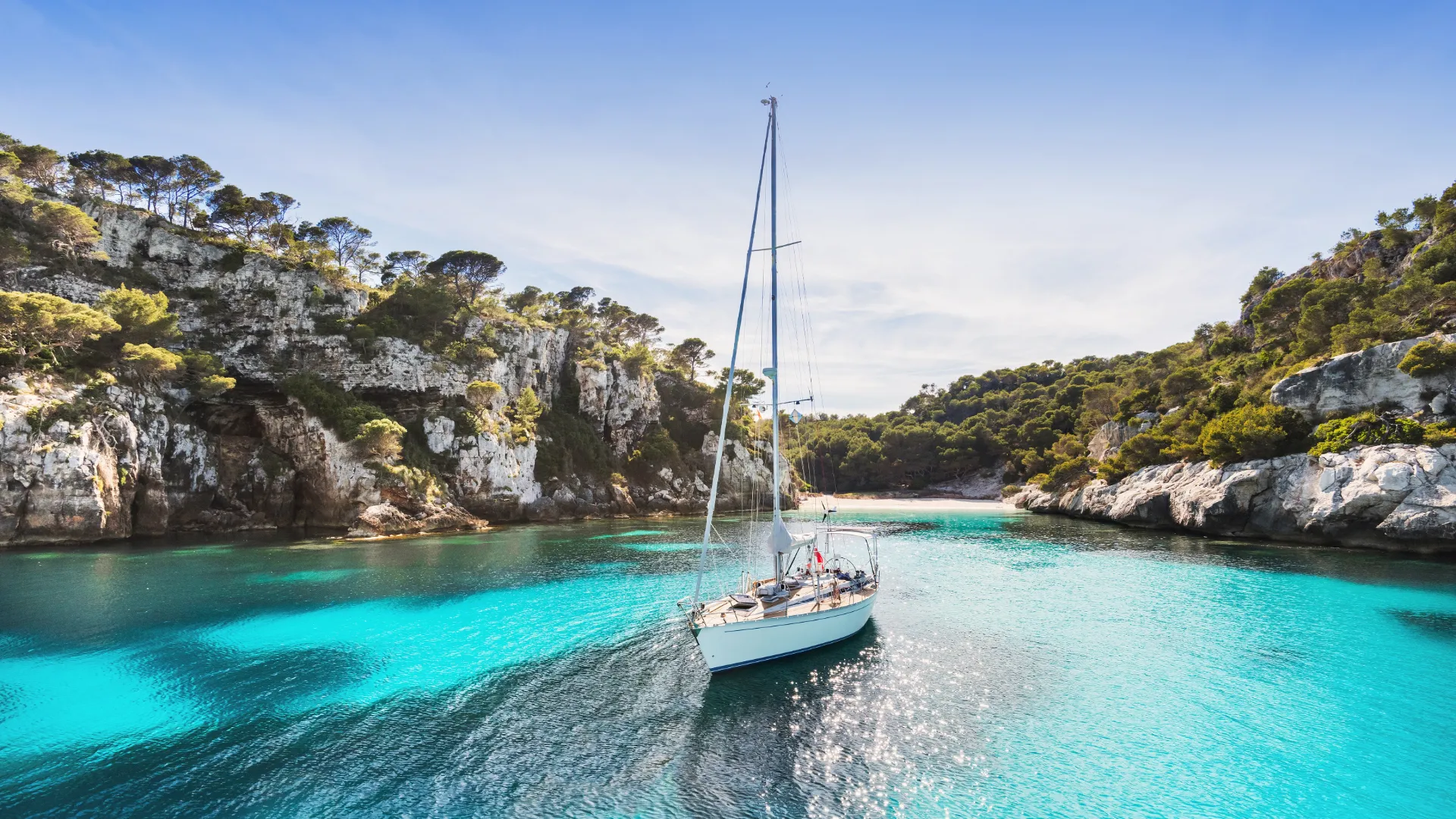 Strand auf Menorca mit Segelboot im Meer.